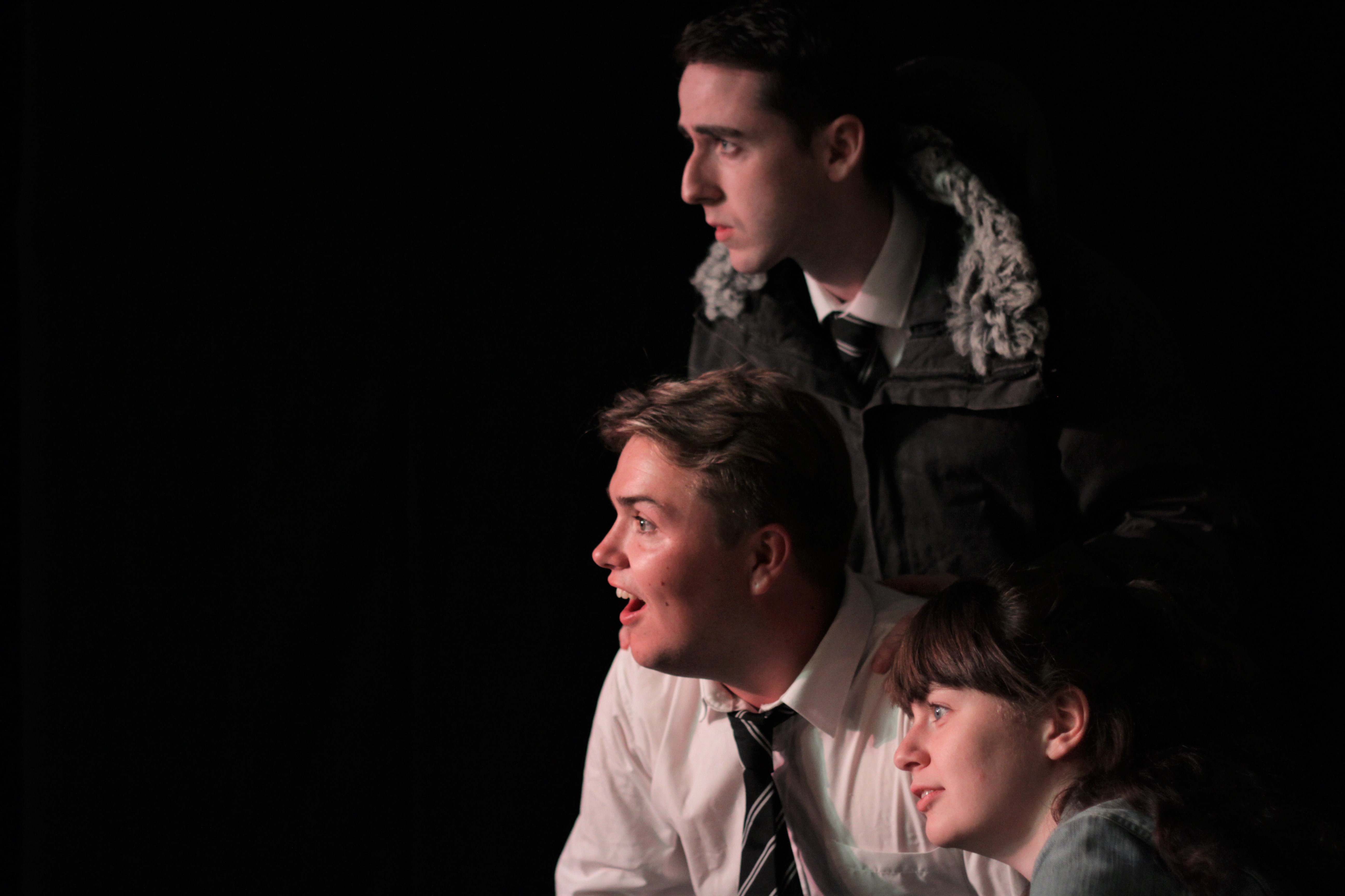 Dark image with actors on the right hand side, looking intently