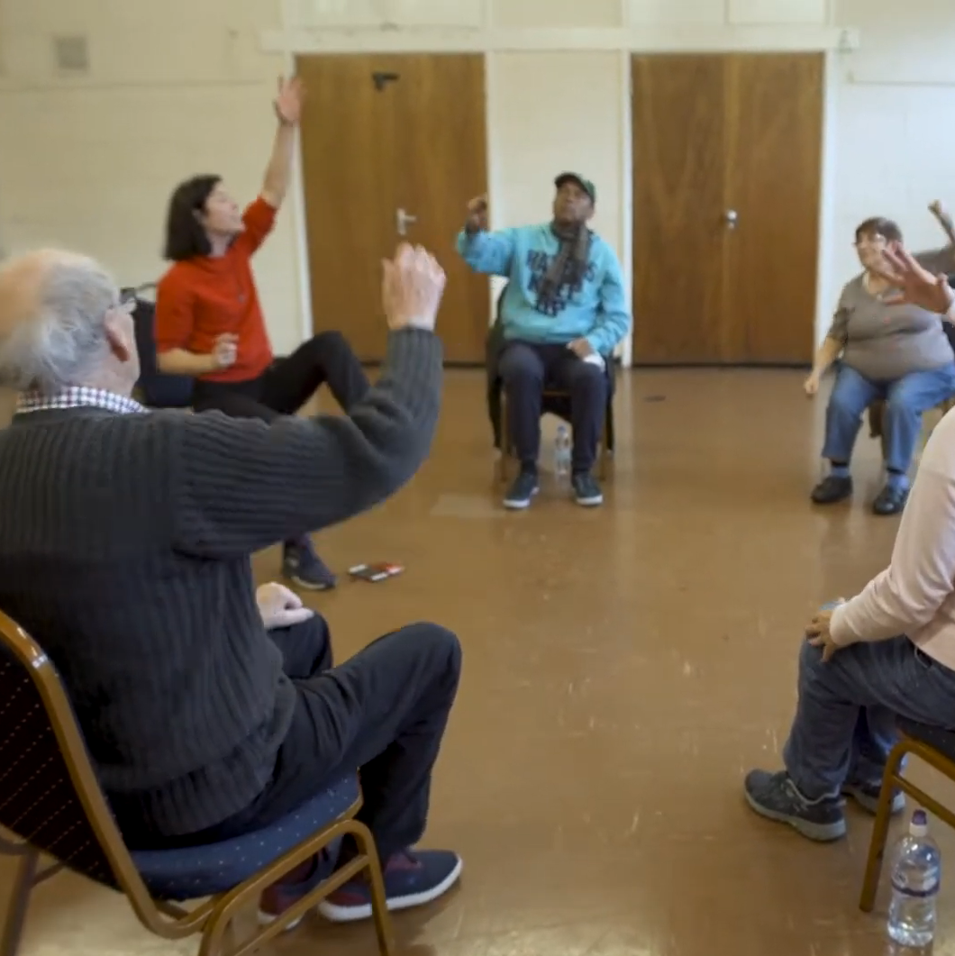 Group of people performing simple exercises whilst seated in chairs.